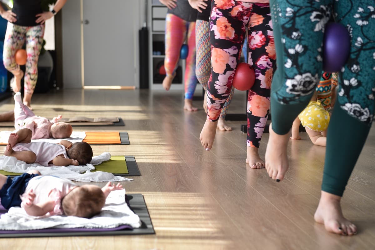 Mums exercising at the barre with babies resting on mats beside them at Evolvere