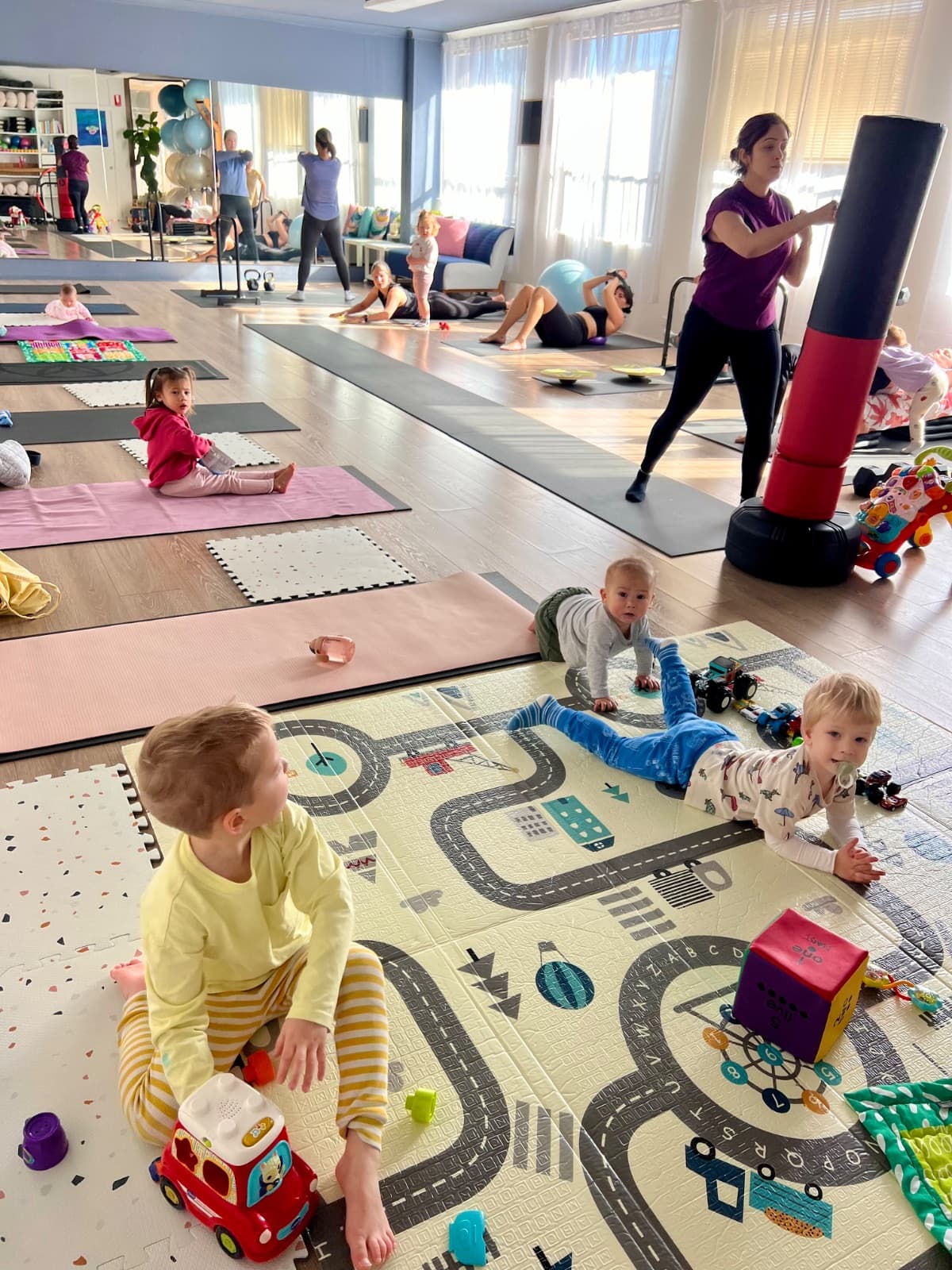 Babies and toddlers playing on mats while mums exercise in the background