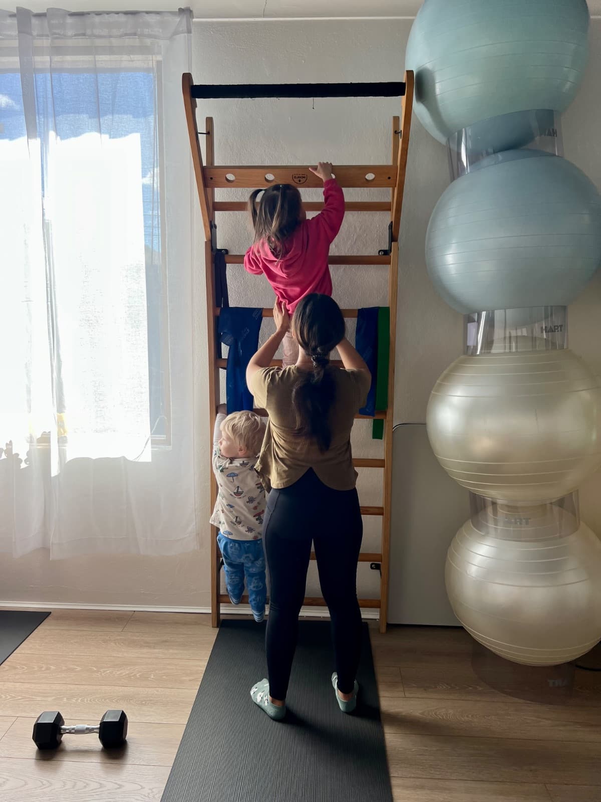 Mum helping child climb the wall bars while toddler watches at Evolvere