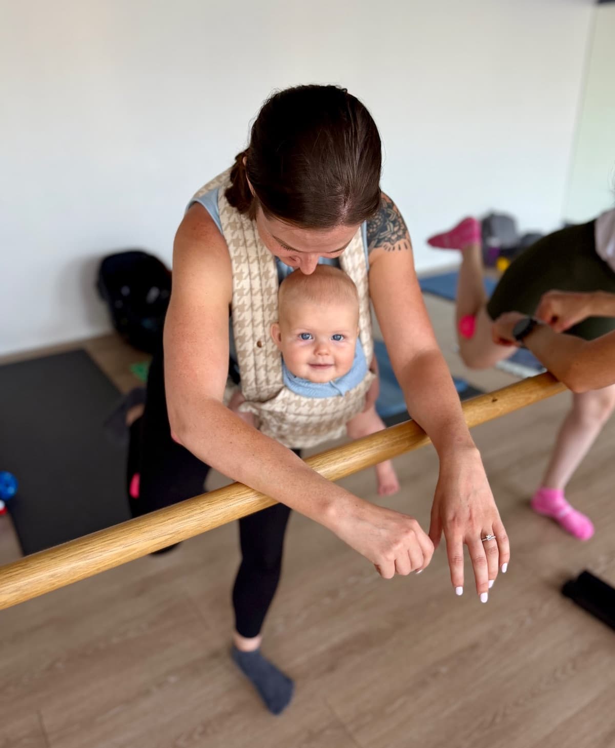 Mum exercising at the barre with baby in a carrier during mums and bubs class