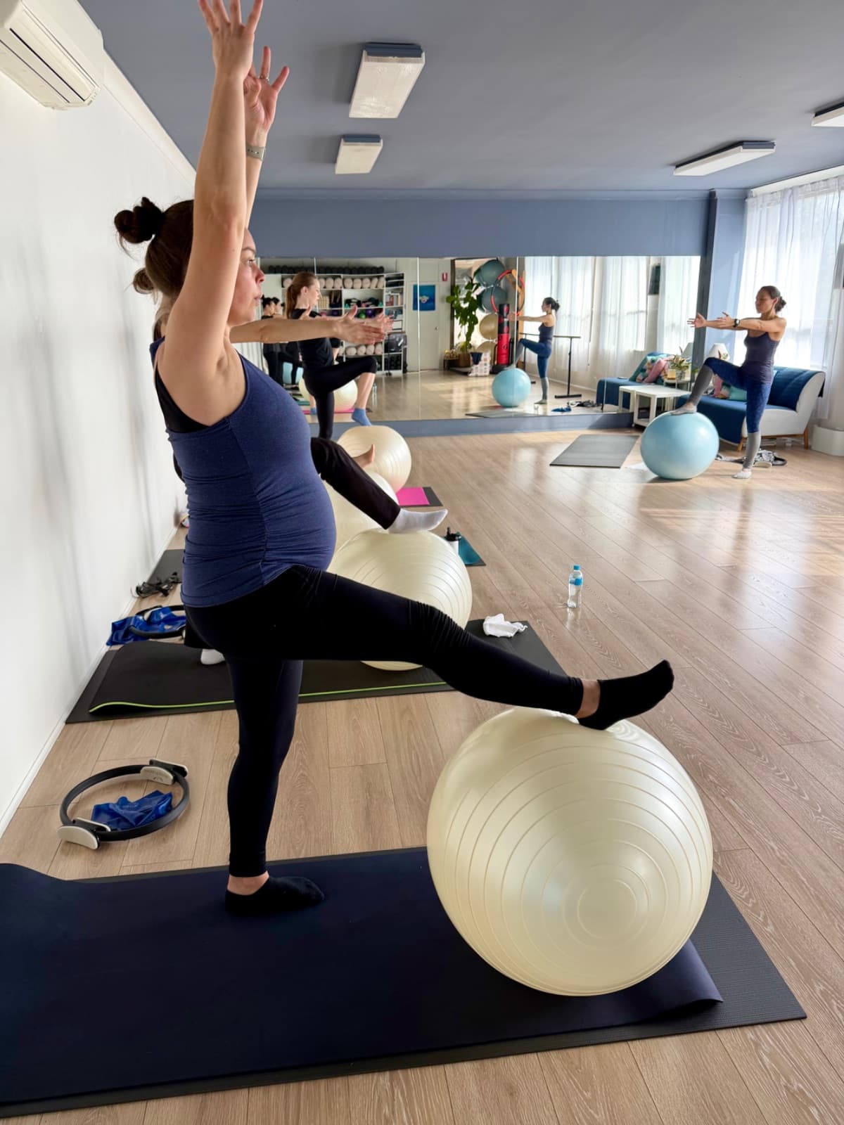 Pregnant woman standing with fitball doing prenatal pilates balance work at the barre