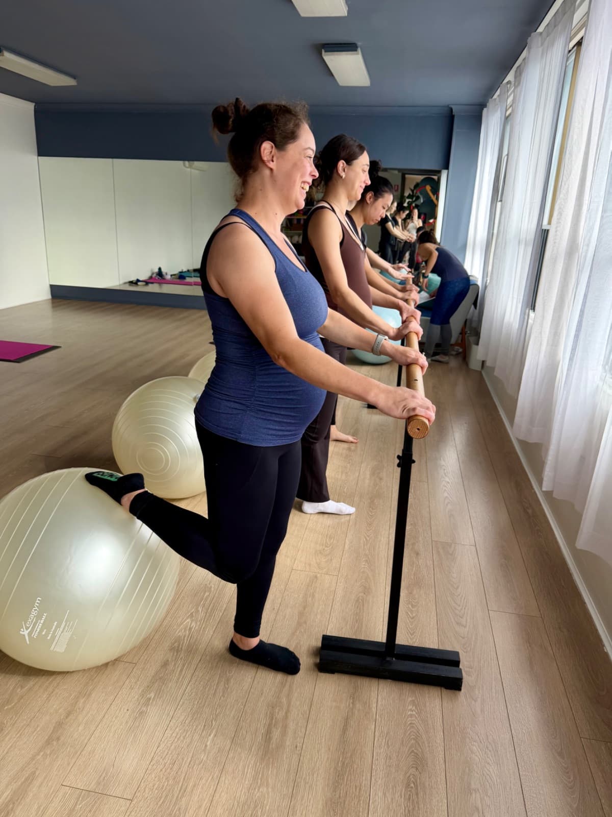 Pregnancy pilates class doing leg extensions at the barre with fitballs