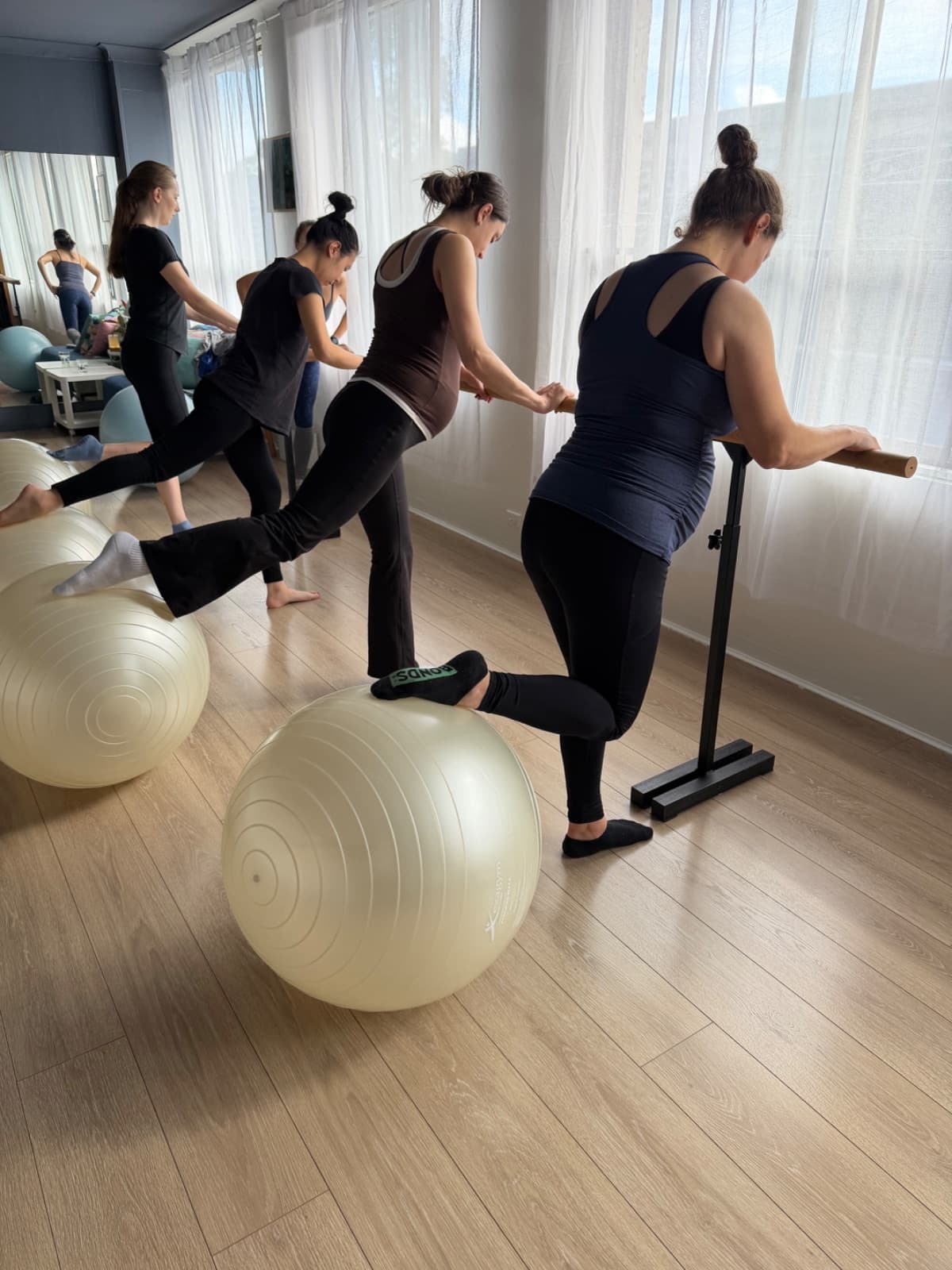 Pregnant women doing supported barre work with fitballs during prenatal pilates